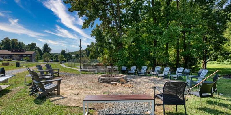 Outdoor firepit area with circle of chairs and surrounding trees.