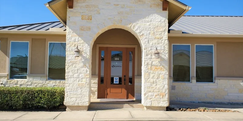 The exterior of Symetria Recovery with a stone entrance and glass doors.
