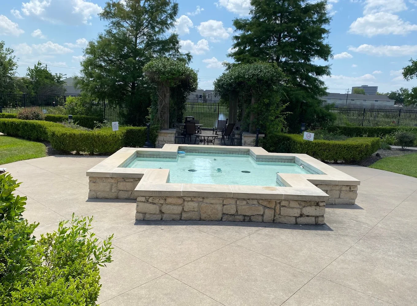 Outdoor area with a fountain around greenery, and a seating area.