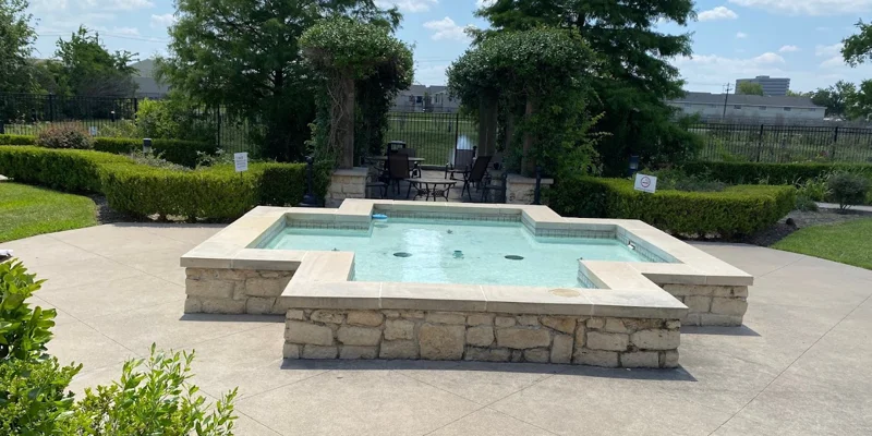 Outdoor area with a fountain around greenery, and a seating area.