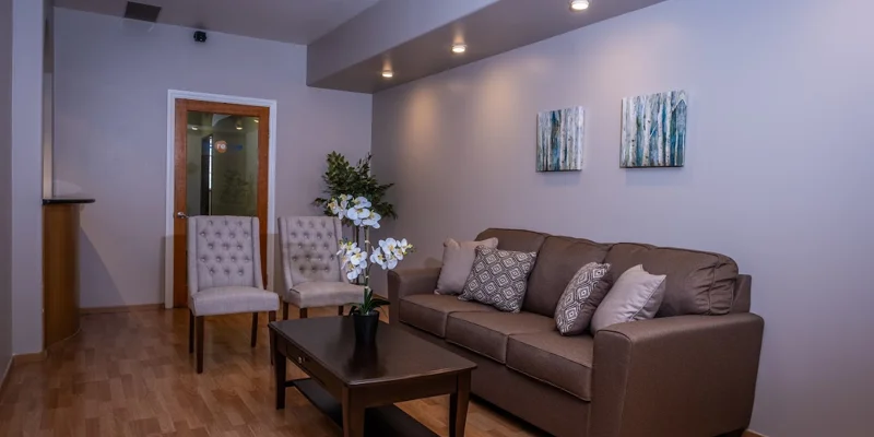 Cozy waiting area with a brown couch, two chairs, and warm lighting.