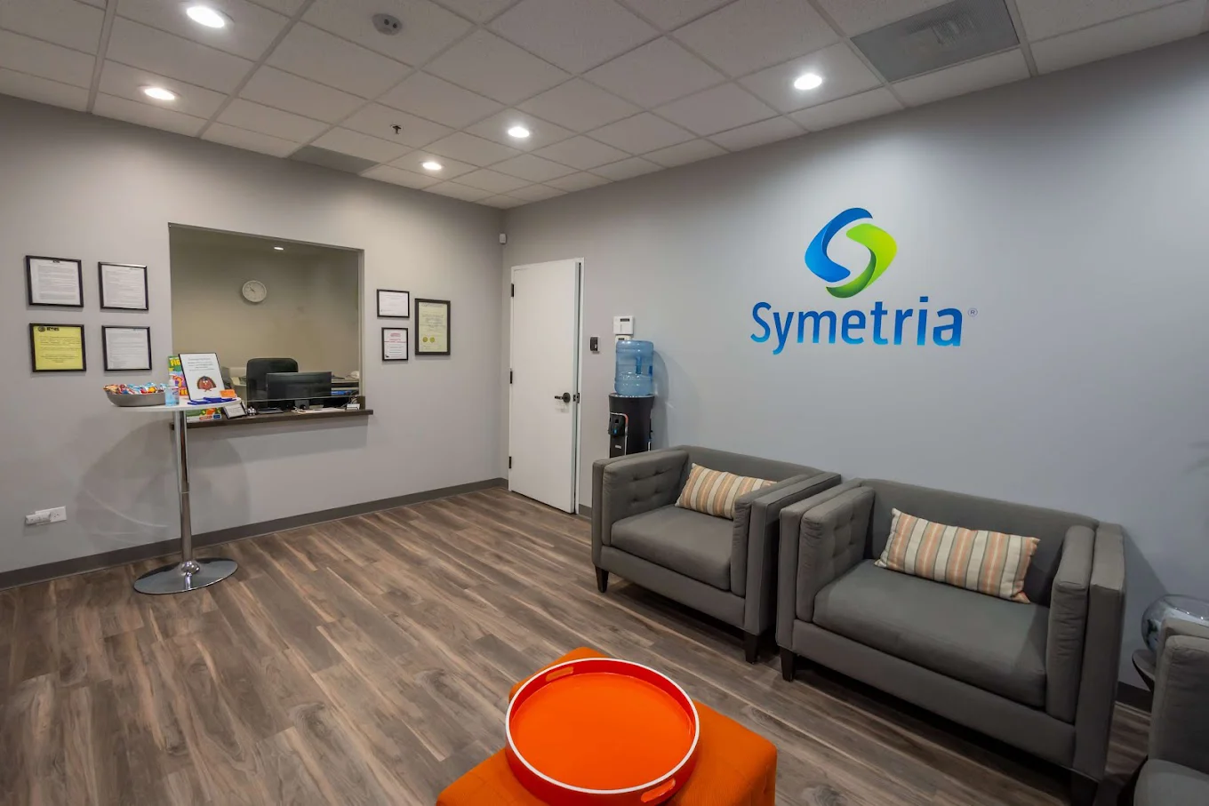 Waiting room with  gray chairs, a water cooler, and the Symetria logo on the wall.
