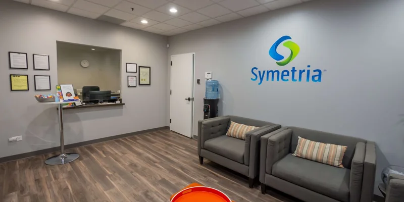 Waiting room with  gray chairs, a water cooler, and the Symetria logo on the wall.