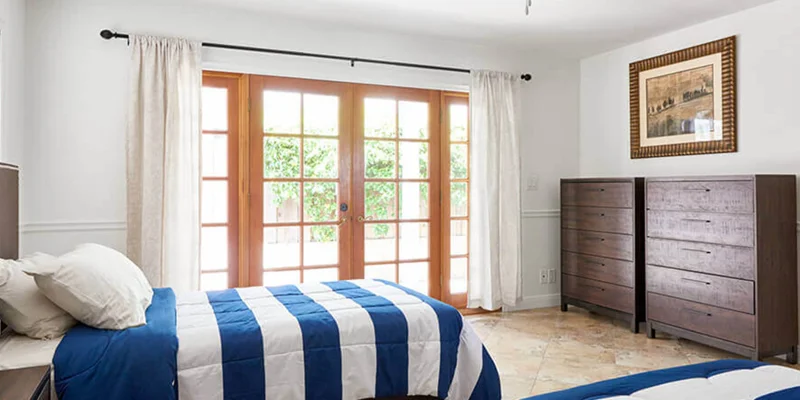 A bedroom with two twin beds, a dresser, and glass doors leading outside.