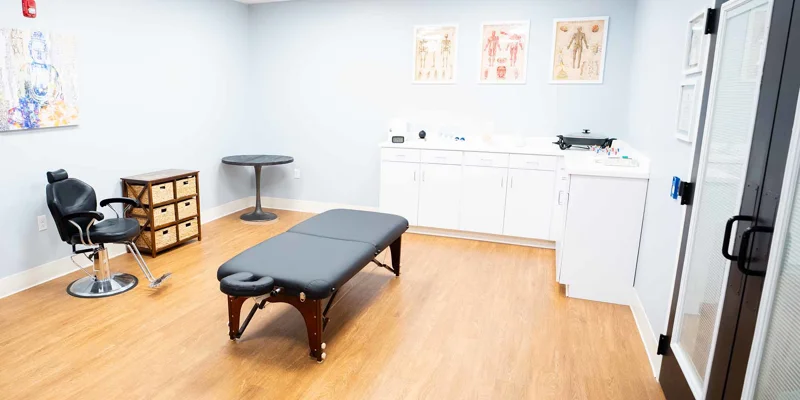 A medical room with a massage table, chair, and cabinets