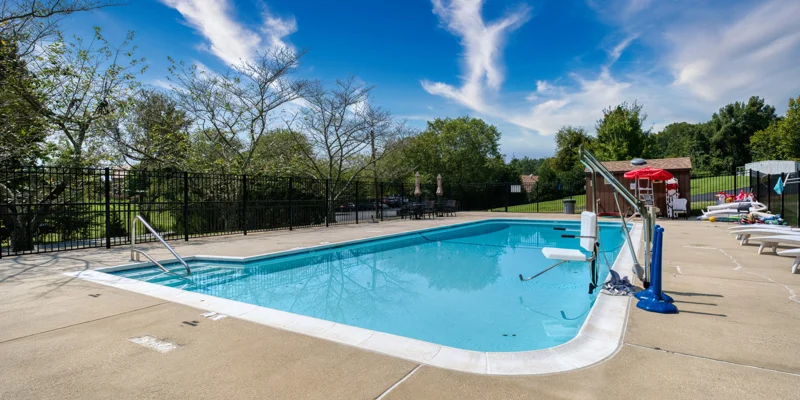 Outdoor swimming pool with lounge chairs and fenced area.