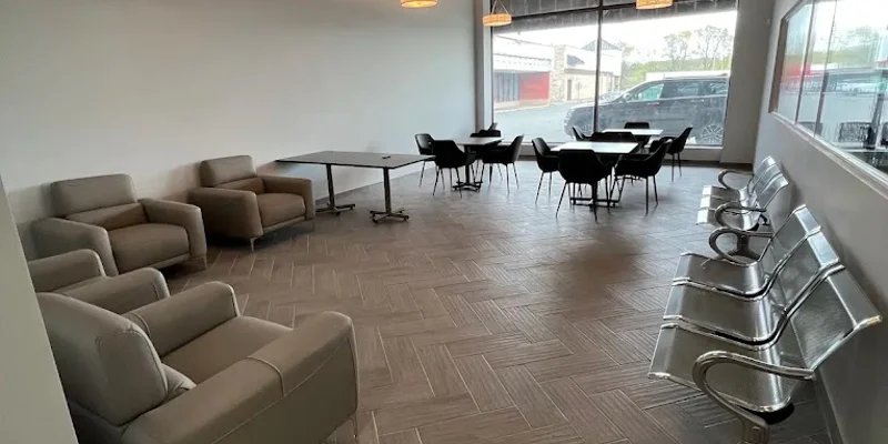 A bright, modern lounge with chairs and tables near large windows.