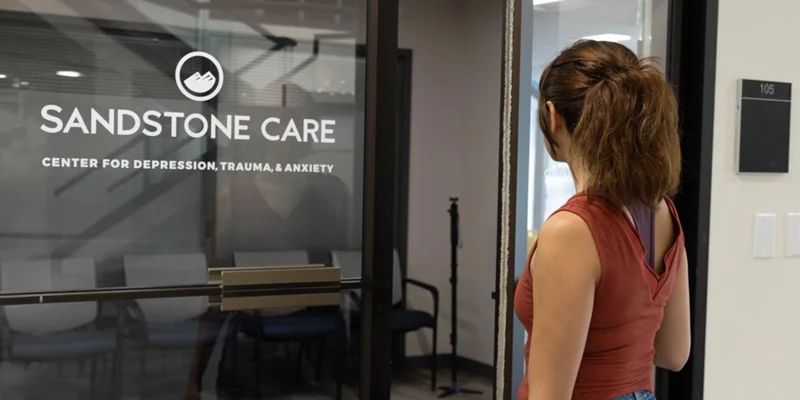 A woman standing outside Sandstone Care’s glass entrance.