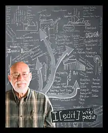 A man says I edit in Wikipedia while standing in front of an educational chalkboard.