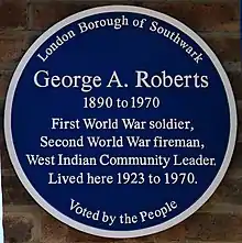 Circular blue plaque, with six lines of text reading "George A. Roberts / 1890 to 1970 / First World War soldier, / Second World War fireman, / West Indian Community Leader / lived here 1923 to 1970". Above those, the text "London Borough of Southwark" and below them, "Voted by the People".