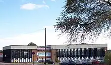 A building approximately 3 stories high. For the most part, the building is made up of horizontal columns of an opaque white panel up to around head height, with 3 windows arranged vertically above this. The columns are approximately 0.5 m (1.6 ft) wide and run from just below the roof to just above ground level and are separated by vertical wooden beams. Above the columns of windows a corrugated white border runs along the top of the building.