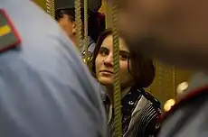 A woman with brown hair and a floral shirt. The view of Samutsevich is obstructed by two uniformed officers standing in front of her.