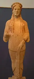 Kore nº 670, del 500&nbsp;a.&nbsp;C., con la expresión facial típica del arte arcaico (la «sonrisa arcaica»). En una mano, llevaría las ofrendas (flores, pájaros, fruta).