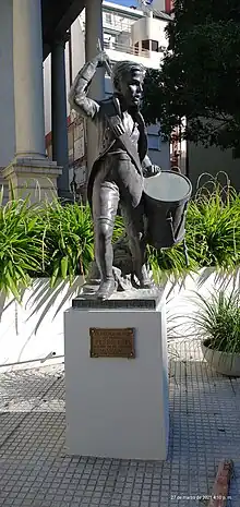 Escultura en bronce con la figura de un niño vistiendo ropas de soldado y portando un tambor.