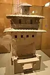 Un modelo de cerámica de una torre silo de grano con ventanas y un balcón colocado varios pisos por encima del patio