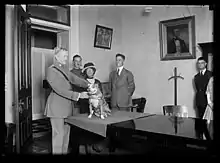 John J. Pershing sosteniendo a su perro el sargento. Stubby, mientras Robert Conroy, vestido de traje, se para detrás de ellos.