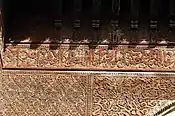 Inscripción con caligrafía árabe tallada en madera en la Madrasa de Sahrij en Fez, rodeada de otra decoración a base de arabescos (principios del siglo&nbsp;XIV)