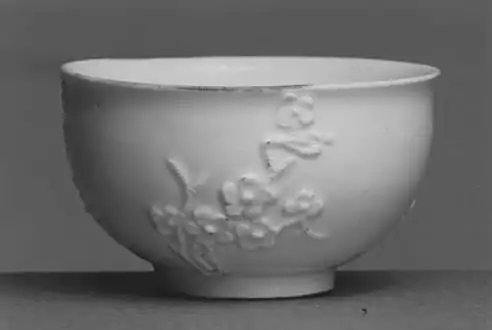 Una copa realizada en la Manufactura de Porcelana de Meissen, Alemania, h. 1725-1730. Aunque conocida en China durante mucho tiempo, la técnica de hacer porcelana auténtica o de pasta dura no se descubrió en Europa hasta los experimentos de J. F. Böttger en Meissen a principios del siglo XVIII. Esta pequeña copa de porcelana con su decoración aplicada de flores de ciruelo u otros árboles Prunus refleja la influencia de un prototipo de porcelana «Blanc de Chine» china.