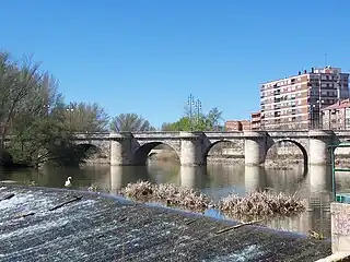 La foto muestra un puente de piedra con cinco arcos sobre el río.