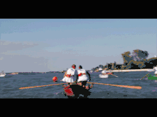 Mujeres que reman en barco rojo, en la laguna de Venecia. Día soleado.  Mujeres vestidas con una camiseta blanca y una minifalda blanca.