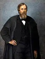 Retrato de medio cuerpo de un hombre maduro, vestido de oscuro, lleva barba. El fondo es gris neutro.