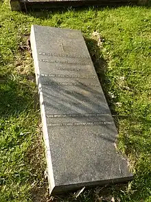 Una lápida horizontal de granito pulido, enmarcada en césped, de unos cuatro pies de largo. En ella se lee: "WILLIAM SCORESBY ROUTLEDGE / AND HIS BELOVED WIFE / KATHARINE ROUNTLEDGE / OF EWERS BURSLEDON / WHO DIED APRIL 13 1939 / AGED 79 AND APRIL 11 1935 / AGED 74. / GOD IS LOVE". En el borde superior de la lápida se encuentra la marca registrada de Edward Taylor de "crisantemos en jarrones" que se encuentra en muchas piedras funerarias de Putney Vale.