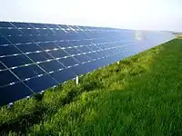 Los paneles solares, con un ángulo de unos 30 grados, reflejan el cielo azul por encima de un campo cubierto de hierba.