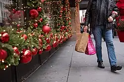 A man carries shopping bags past red and green Christmas decorations