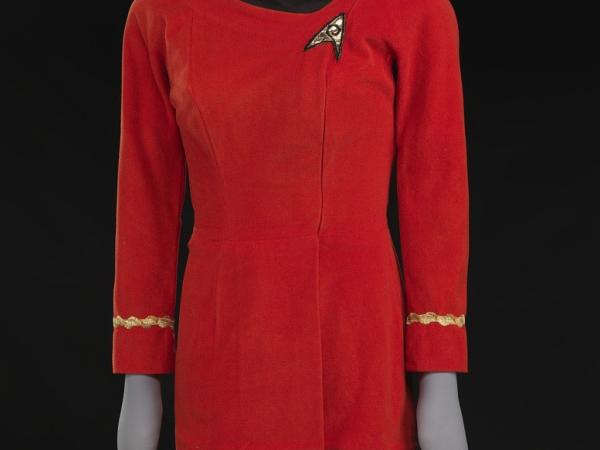 Red dress on a mannequin with gold arm band at sleeves and a wide black collar. On one side of the chest there's a Starfleet logo patch with gold fabric and black embroidery.