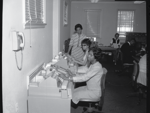 Female bank employees sitting and typing on machines.