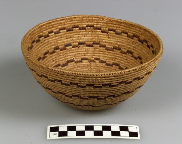 A basket bowl made from tightly coiled material with zig-zagging brown horizontal designs on it.