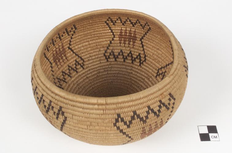 A basket bowl made from tightly coiled material with black and red designs on it.