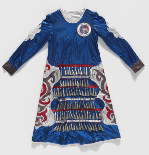 Blue dress made of shiny synthetic fabric with metal bells across the skirt. Above the left breast sits a patch that reads "Never Forgotten SPC Lori Piestewa."