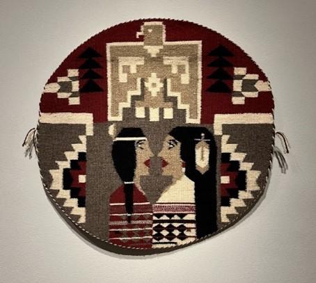 A round rug depicting an eagle on the top protecting a Diné (Navajo) couple.