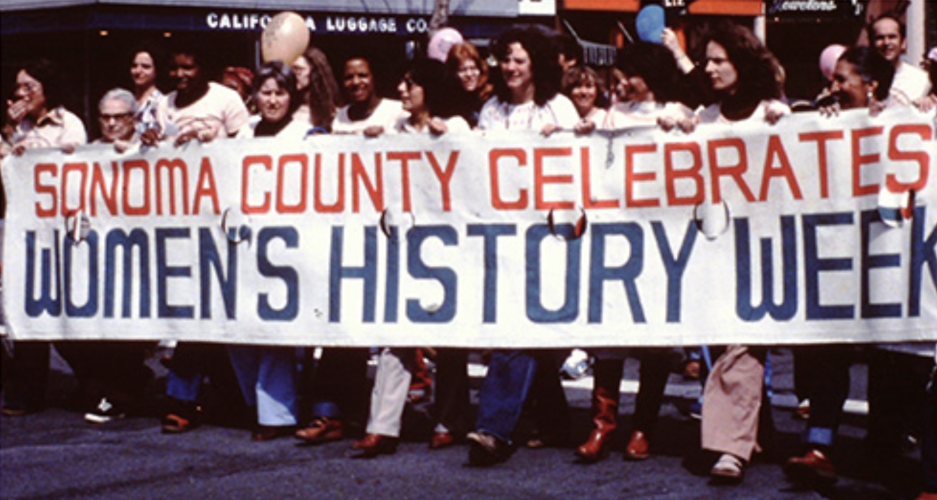A group of women walking in a line holding a banner that reads “Sonoma County Celebrates Women’s History Week.
