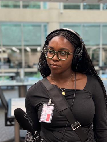 Lena DoDoo with headphones on and holding a microphone pointed towards someone out of frame. 