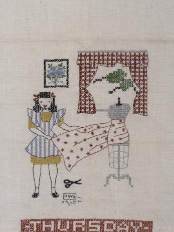 Girl holds piece of starry fabric on a female sewing dress form. She has pins in her mouth, and more pins and a scissors lie on the ground next to her. There is a curtain and a painting behind her.