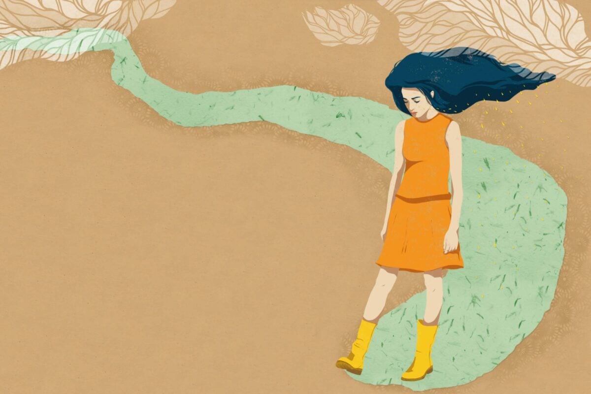 A woman in an orange dress strolls gracefully along a scenic path surrounded by greenery as she is coping with depression.